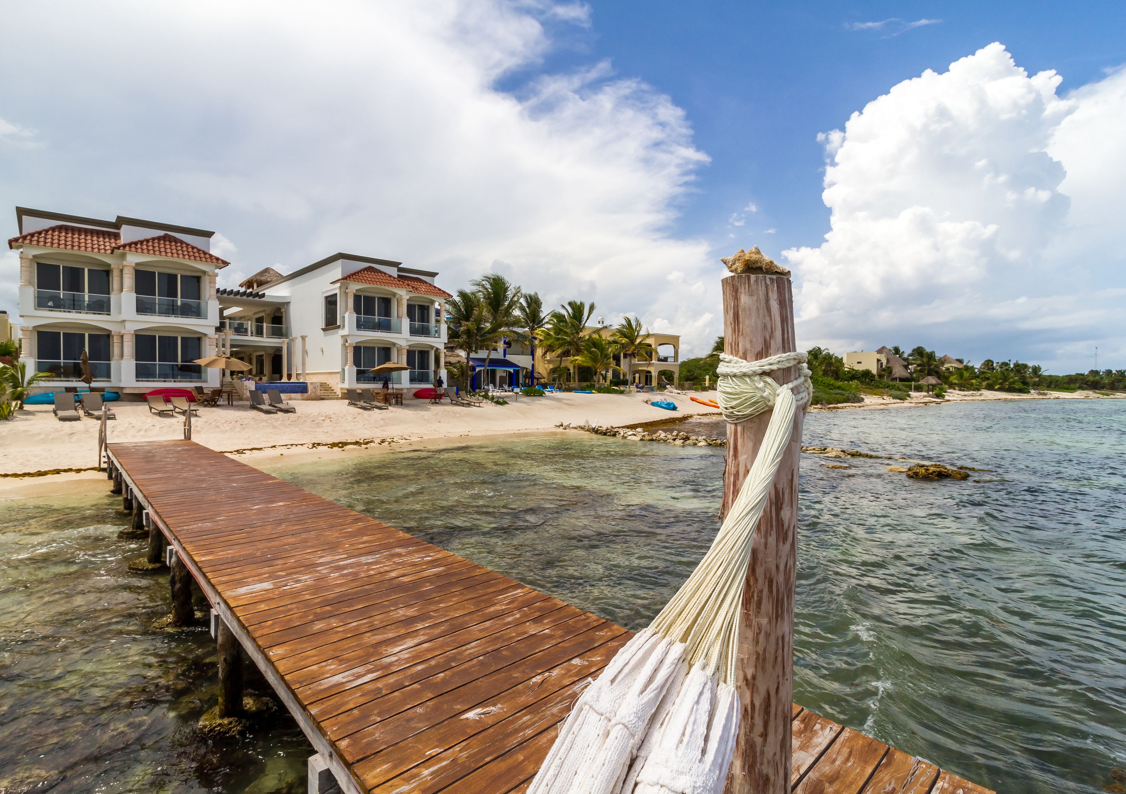 A wooden pier leading to a beach with a row of houses in the background.