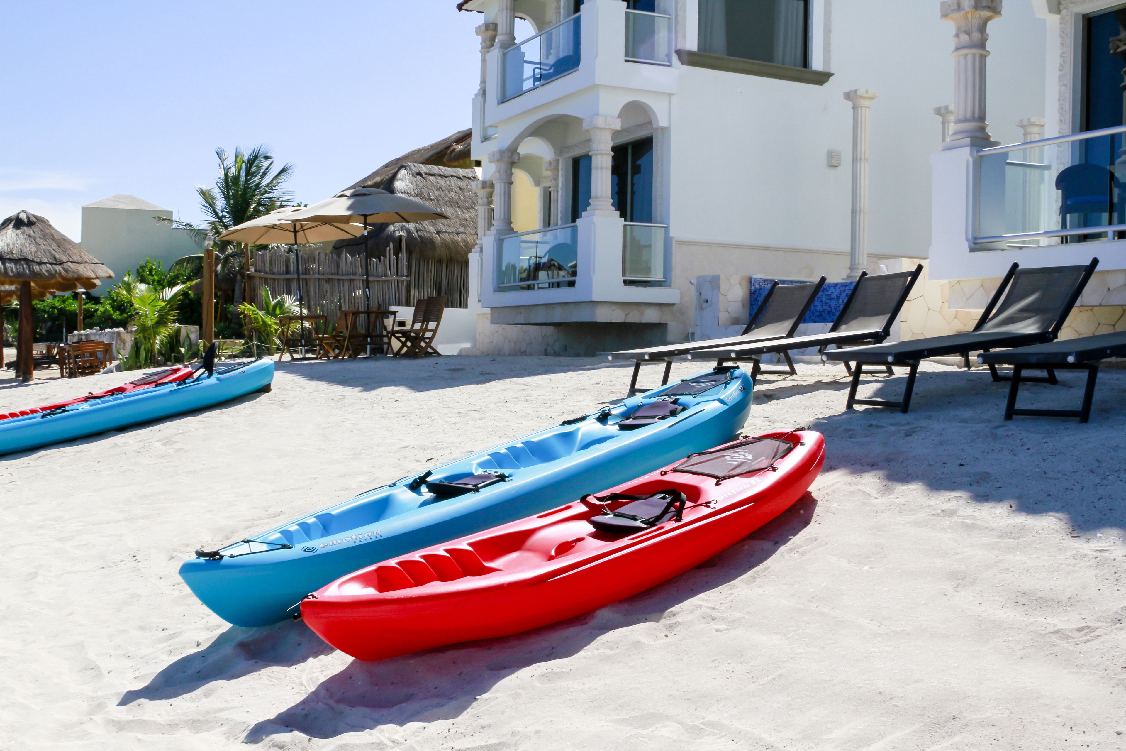 Zona de playa con kayaks, sillas de descanso y un edificio con balcones.