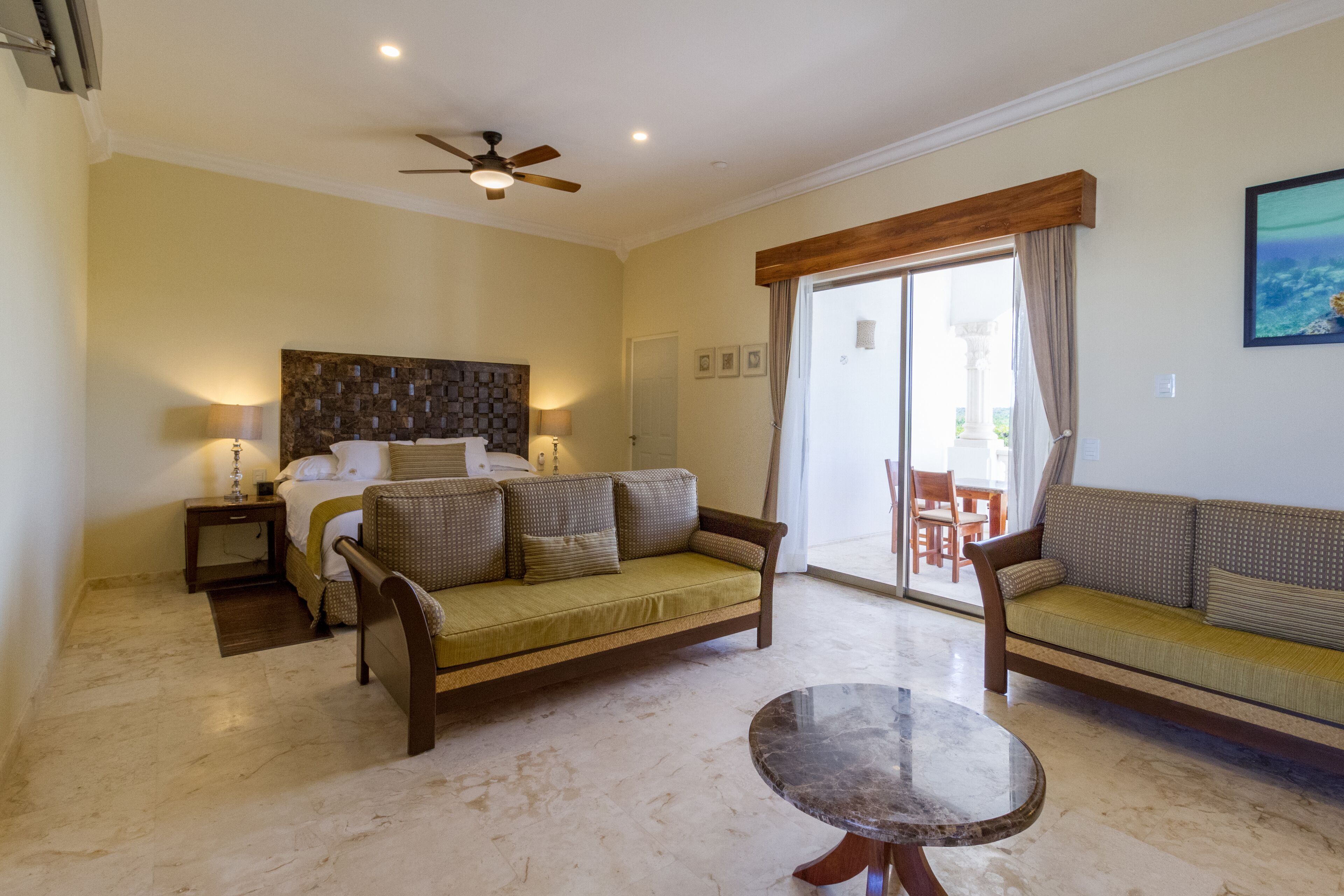 A hotel room with a bed, two sofas, a round table, and a ceiling fan.