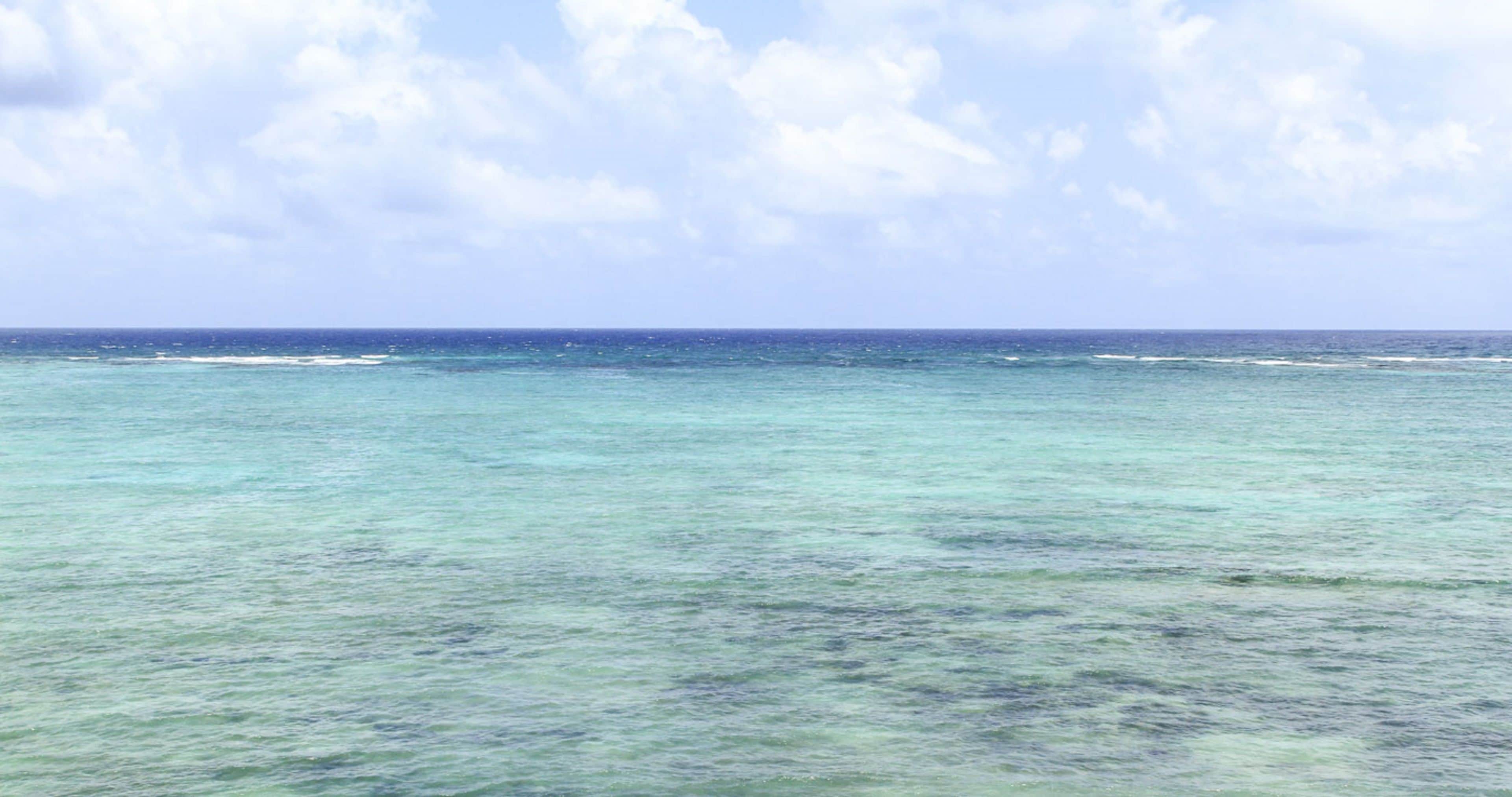 Blick auf einen Strand mit klarem türkisblauem Wasser und einem bewölkten Himmel.