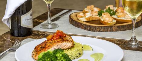 A plate of grilled chicken with broccoli and a lime wedge, accompanied by a bottle of wine and glasses.