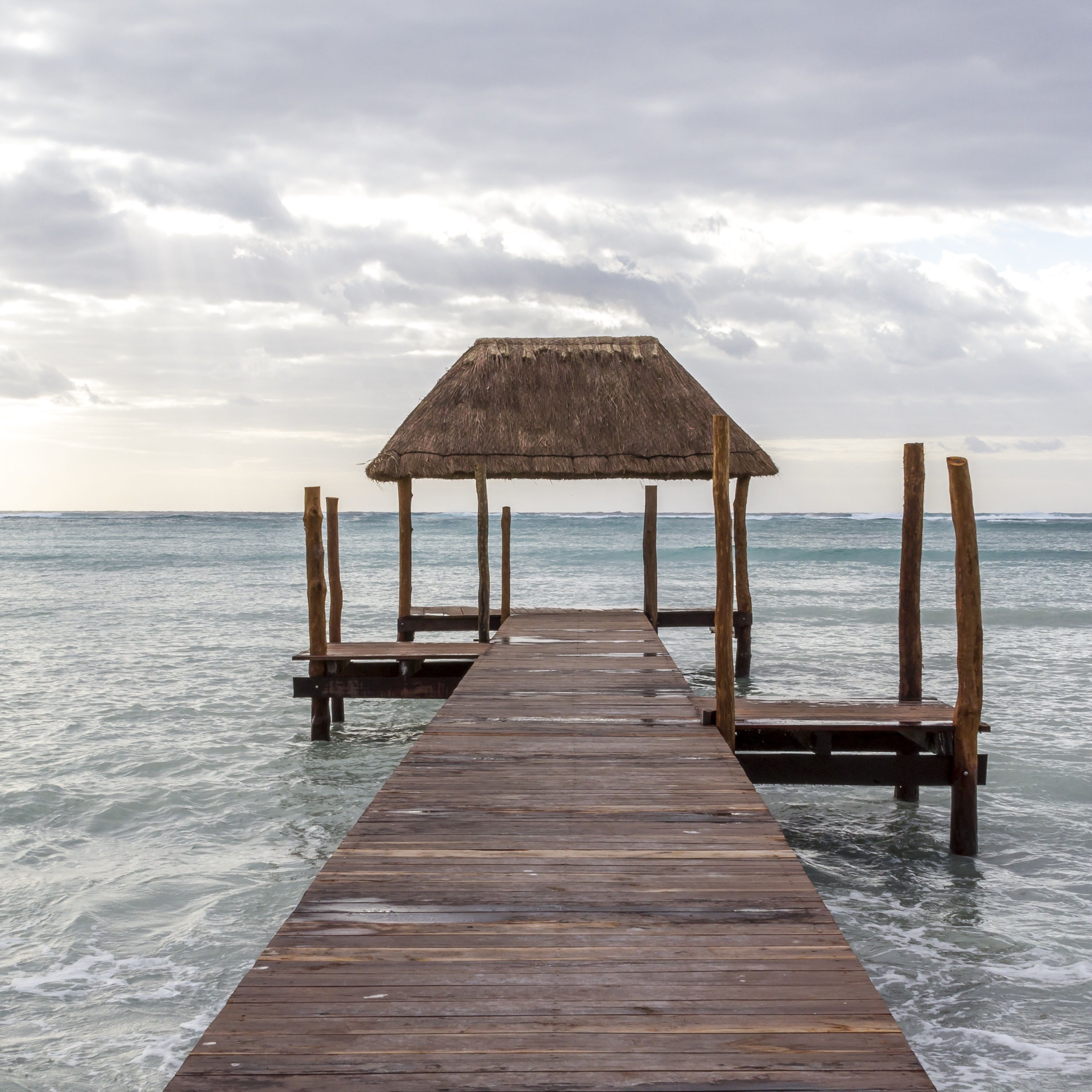 A wooden pier leading to a thatched-roof structure over water.
