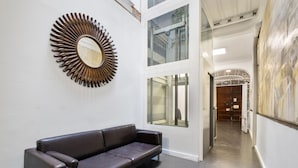 A modern interior with a leather sofa, a sunburst mirror, and a view of a hallway leading to a door. - Hotel Málaga City Suites (Málaga)