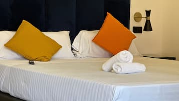 Habitación de hotel con una cama bien hecha, dos almohadas, un control remoto y una toalla enrollada sobre la cama.