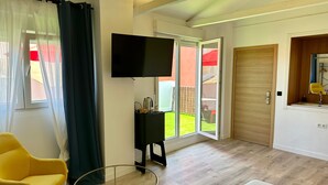 A modern room with a television, a small table, a yellow chair, and a sliding glass door leading to a garden. - Hotel Málaga City Suites (Málaga)