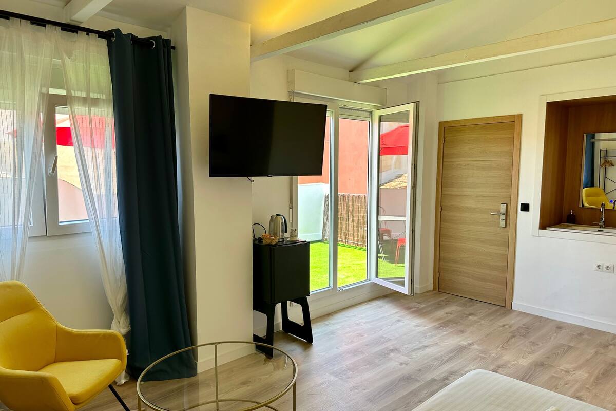 Ein modernes Zimmer mit Fernseher, einem kleinen Tisch, einem gelben Sessel und einer Glasschiebetür, die zu einem Garten führt.