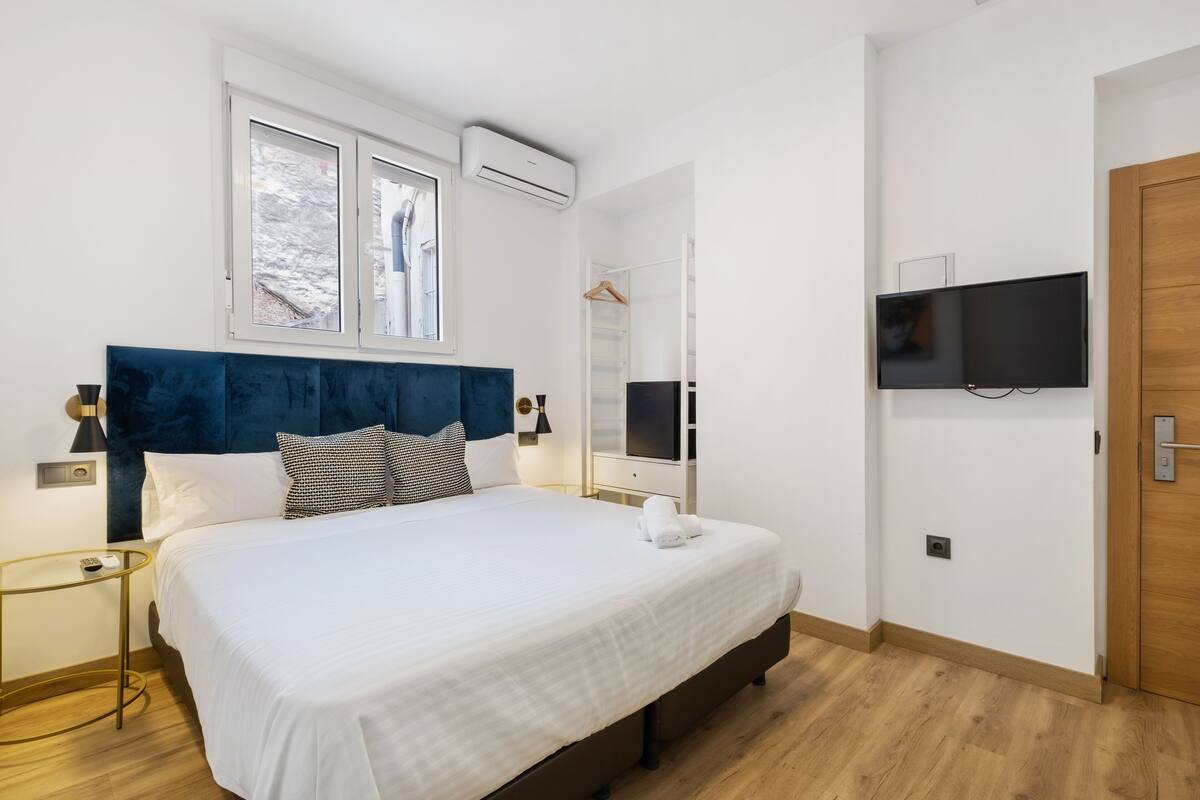 Ein modernes Schlafzimmer mit einem großen Bett, einem an der Wand montierten Fernseher und einem Kleiderschrank.
