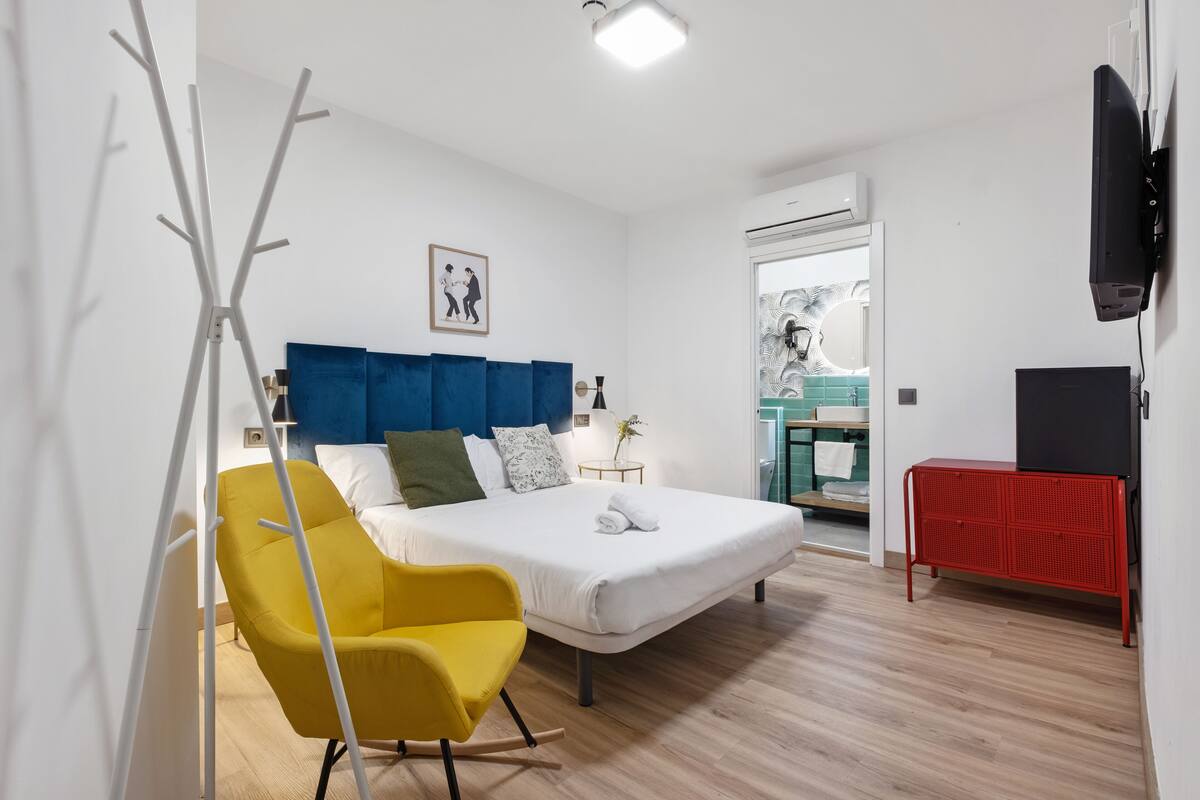 Ein modernes Hotelzimmer mit einem großen Bett, einem gelben Sessel, einem roten Schrank und einem Fernseher.