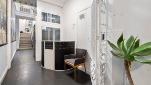 A hallway with a staircase, a wicker chair, a potted plant, and a white door. - Hotel Málaga City Suites (Málaga)