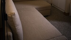 A hotel room with a sofa, a lamp, a window with sheer curtains, and a wardrobe.