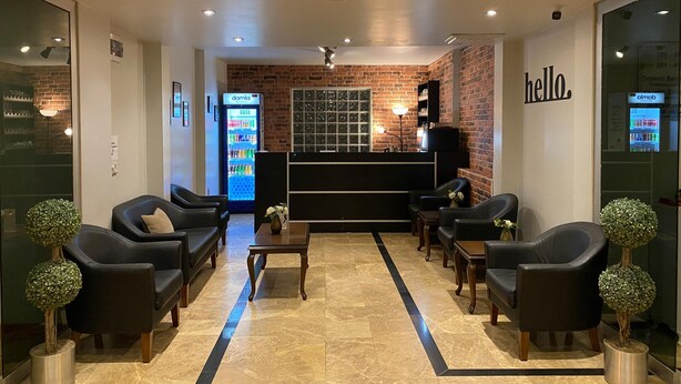 A reception area with a brick wall, a 'hello' sign, a refrigerator, and seating arrangements.