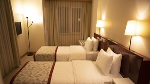 A hotel room with two beds, a bedside table, a lamp, a floor lamp, and a curtain.