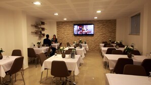 A conference room with multiple tables and chairs, a television screen on the wall, and a brick wall.