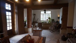 A spacious room with a wooden table and chairs, a brick column, and a window with hanging plants. - Can Ribalta Hotel Gastronòmic (Sant Antoni de Vilamajor)