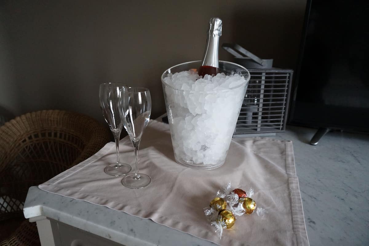 A table with a champagne bottle in an ice bucket, two glasses, and wrapped chocolates.