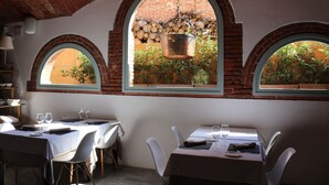 A dining area with tables set for two, arched windows, and a hanging pot. - Can Ribalta Hotel Gastronòmic (Sant Antoni de Vilamajor)