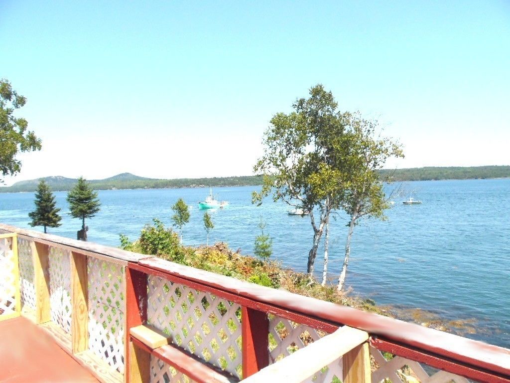 A wooden deck with a lattice railing overlooking a lake with boats and trees.
