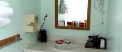 A bathroom with a white sink, a mirror, a hairdryer, and a trash bin.