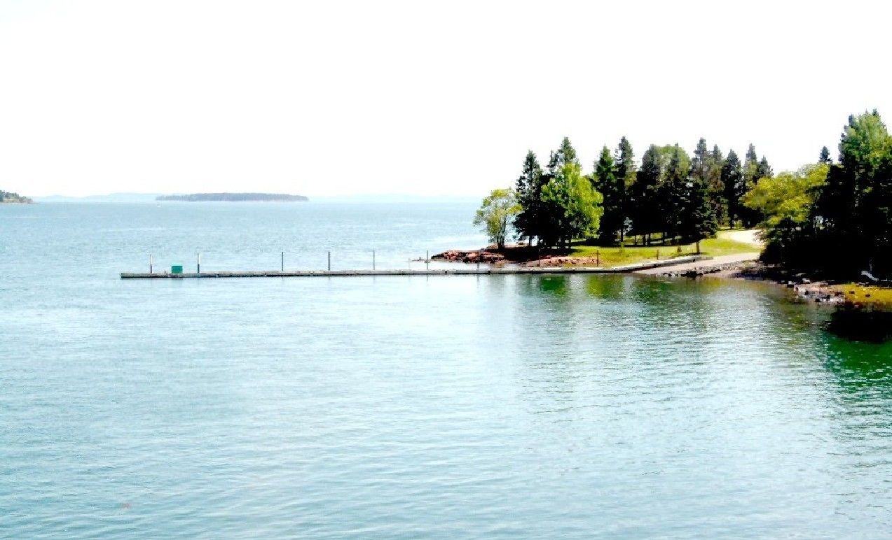 A calm lake with a dock extending into the water, surrounded by trees and a distant shoreline.