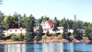 Une grande maison avec un toit rouge, entourée d’arbres et bordée par un plan d’eau.