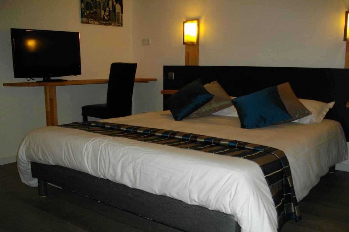 A hotel room with a bed, a desk with a television, and two wall-mounted lights.