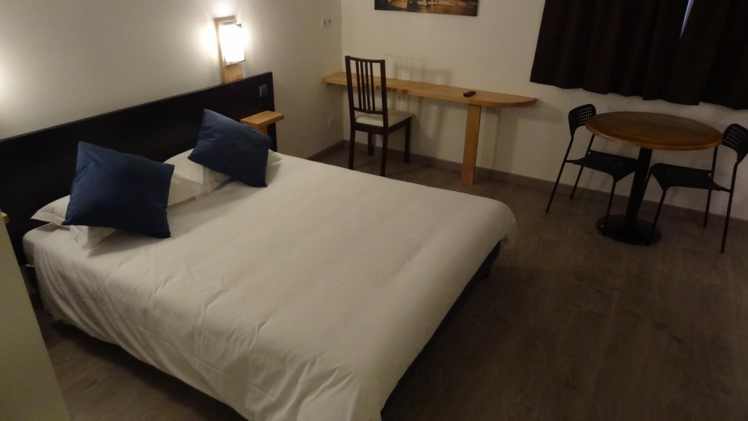 A hotel room with a bed, a desk, two chairs, and a small table.