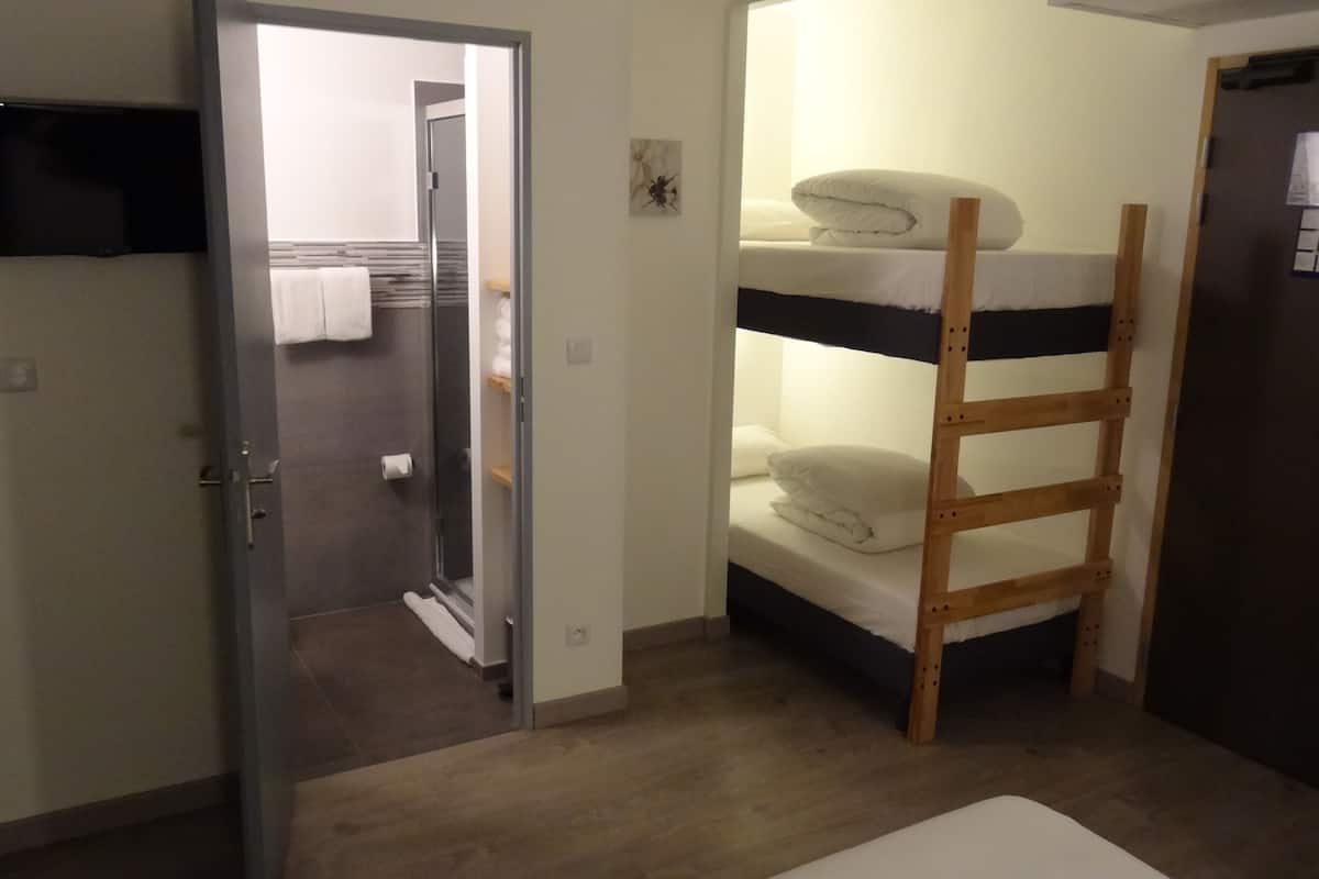 A room with a bunk bed, a door, a towel rack, and a flat-screen TV mounted on the wall.