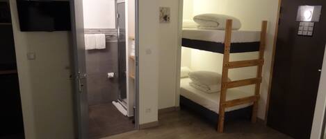 Une chambre avec un lit superposé, une porte, un porte-serviettes et un téléviseur à écran plat fixé au mur.