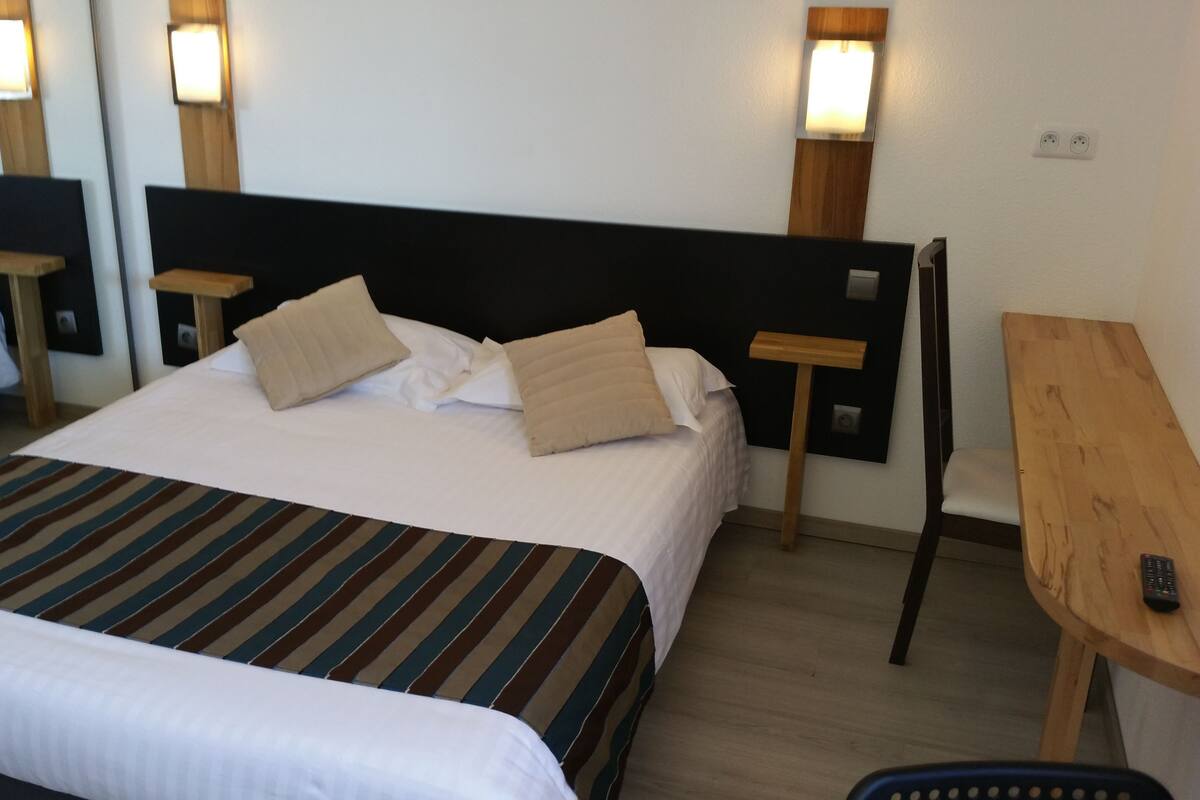 A hotel room with a bed, bedside tables, a desk, and a chair.