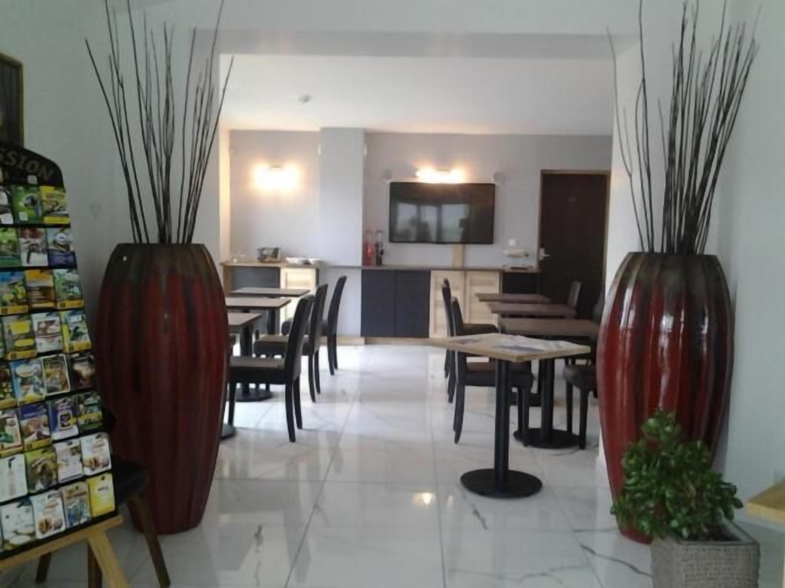 A modern dining area with a kitchen in the background, featuring a TV mounted on the wall and a small bar area.