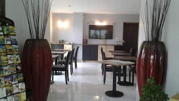 A modern dining area with a kitchen in the background, featuring a TV mounted on the wall and a small bar area.