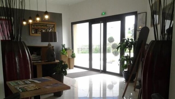 En moderne lobby med en reception, potteplanter og en stor glasdør, der fører udendørs.