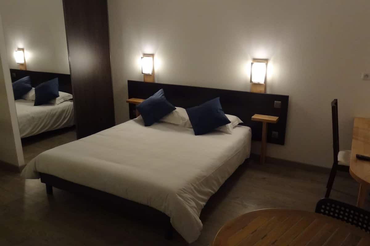 A hotel room with a bed, bedside tables, a chair, and a small table.