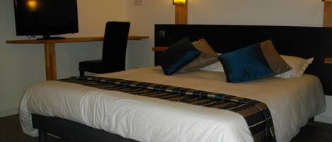 A hotel room with a bed, a desk with a television, and two wall-mounted lights.