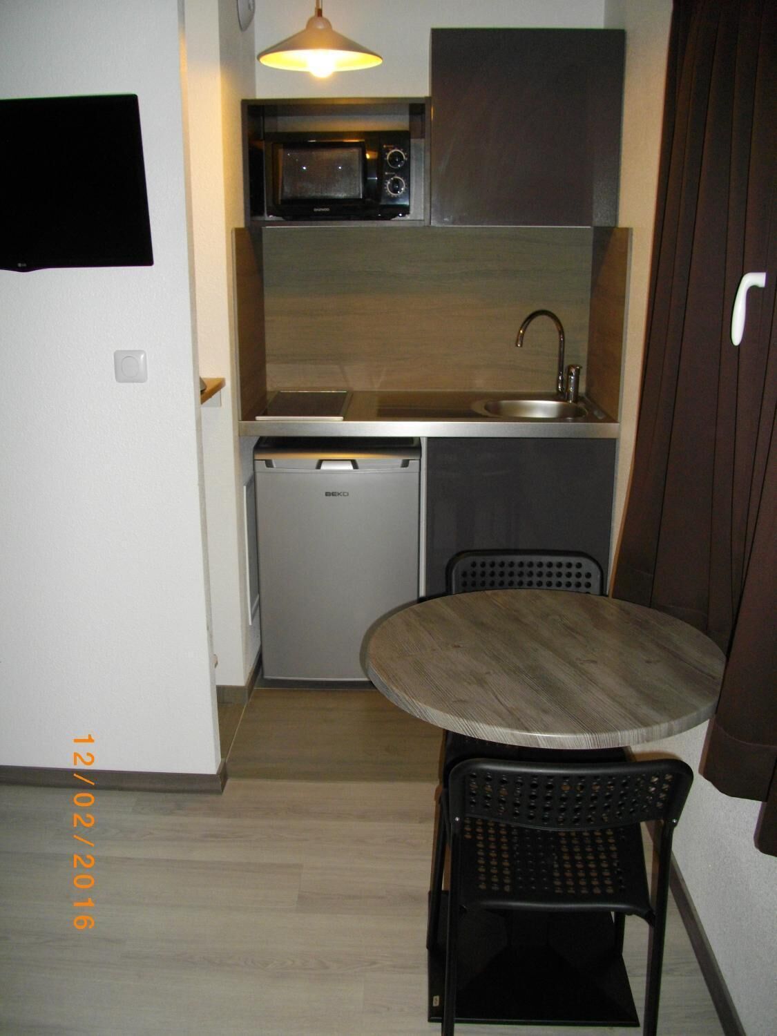 A compact kitchen with a microwave, sink, and a small dishwasher. There's a round table with two chairs and a hanging light fixture above.
