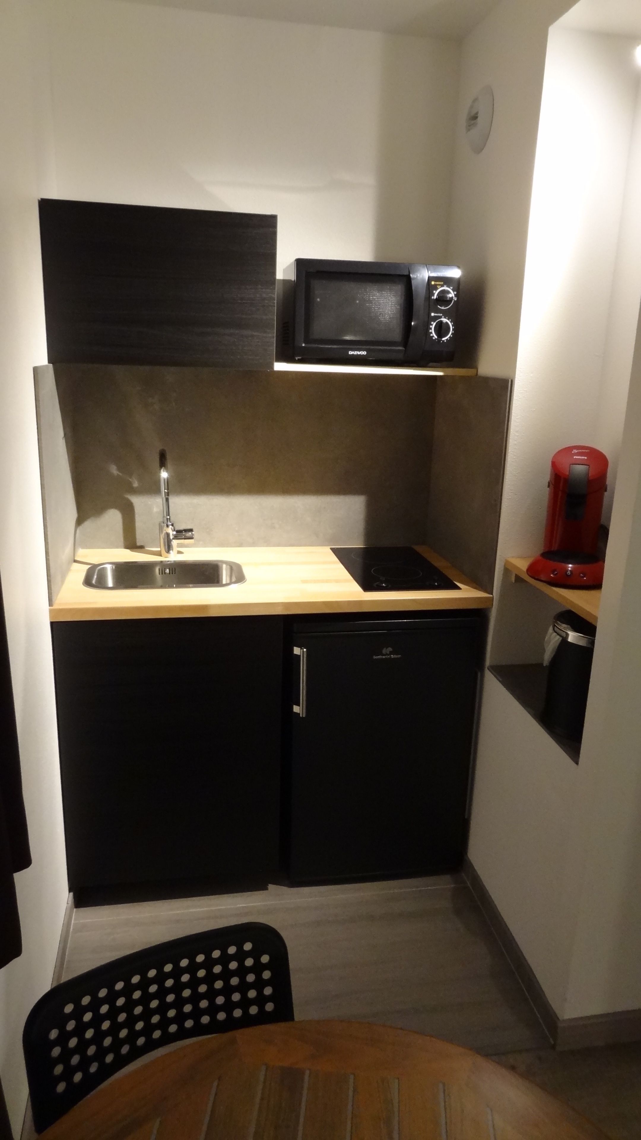 Una cocina compacta con microondas, lavamanos y cafetera.
