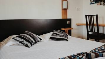 A neatly made bed with striped pillows and a striped blanket, a wooden nightstand with a lamp, and a chair.