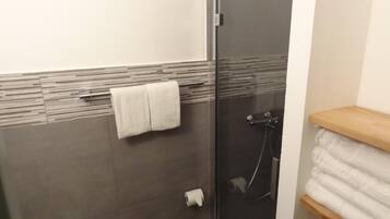 A bathroom with a glass shower enclosure, a towel rack with two towels, and a toilet paper roll on the floor.