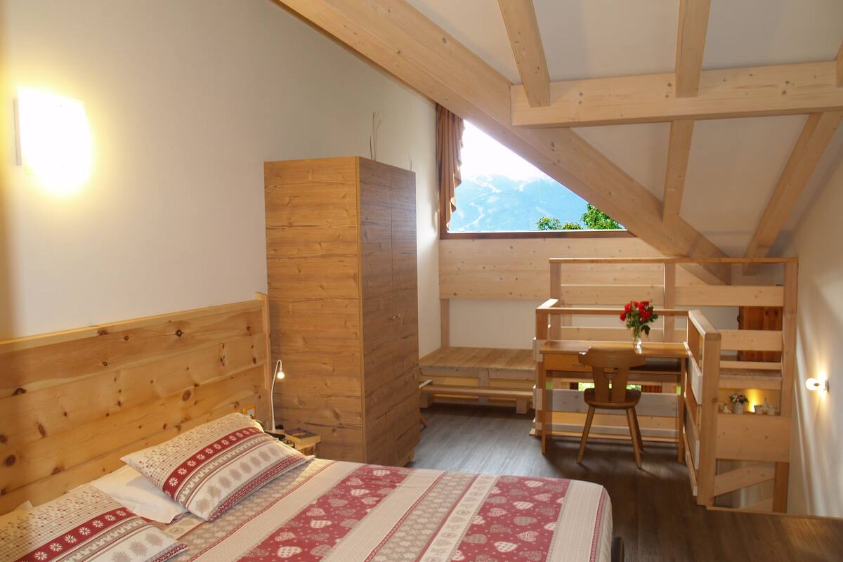 Une chambre avec un lit en bois, un bureau et une fenêtre donnant sur la montagne.