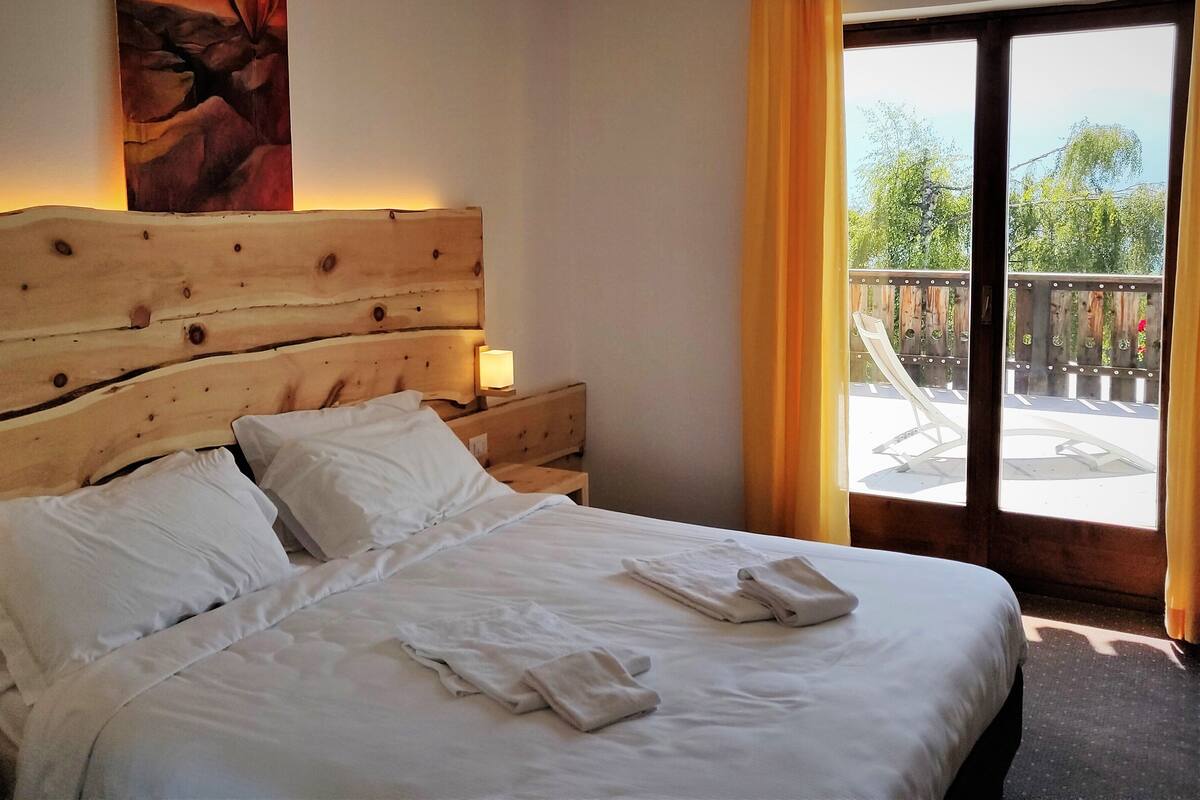 Un lit bien fait, avec du linge de lit blanc, une tête de lit en bois et une petite table de chevet surmontée d’une lampe.