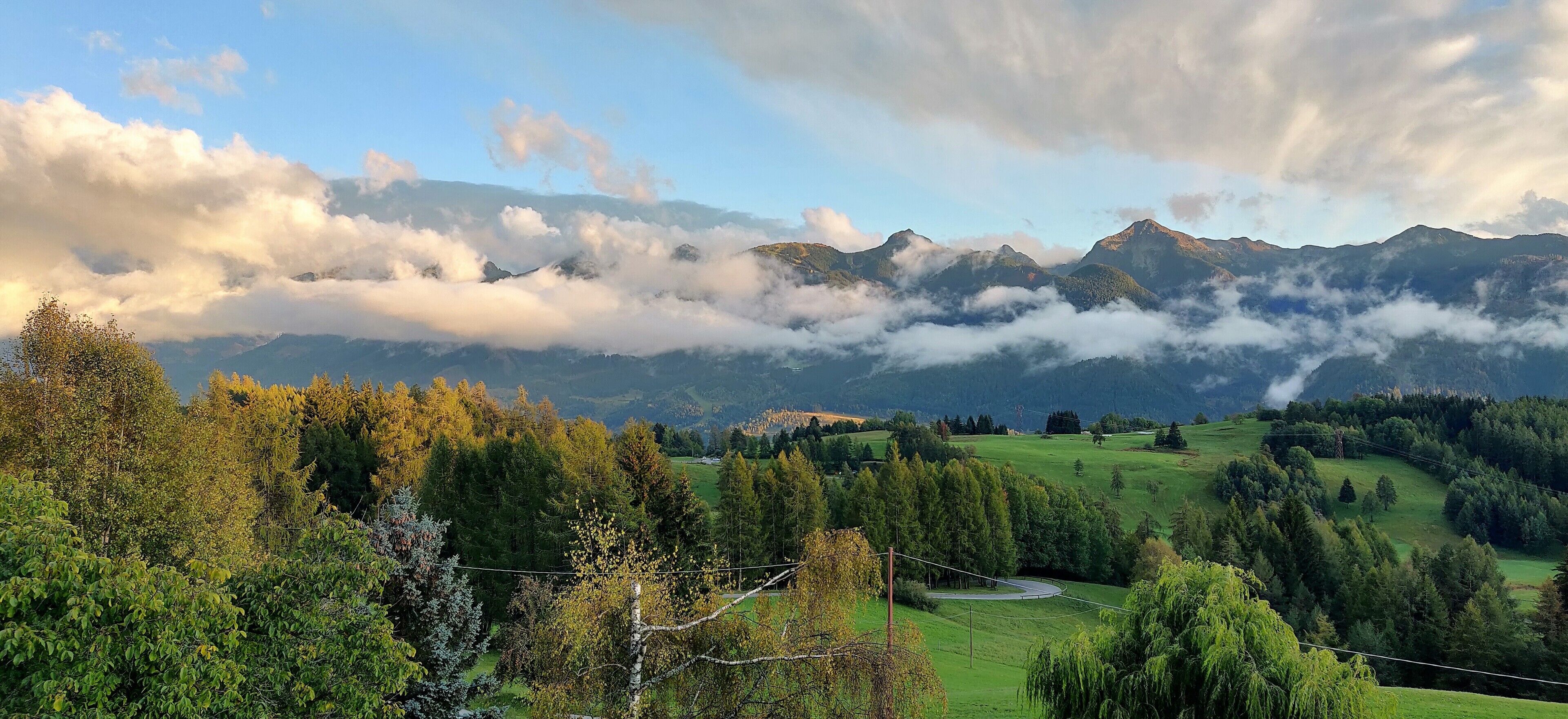 A mountainous landscape with a winding road, lush greenery, and a clear sky.
