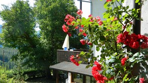 Une terrasse en bois avec une table et des chaises, entourée d’une végétation luxuriante et de fleurs rouges.