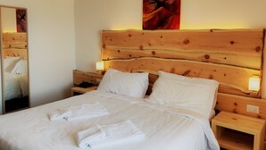 Un lit bien fait, avec du linge de lit et des serviettes blanches, une tête de lit en bois, des lampes de chevet et un tableau au mur.