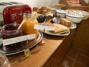 Ein Buffet mit verschiedenen Speisen, darunter ein roter Toaster, Gläser mit Marmelade und beschriftete Teller.