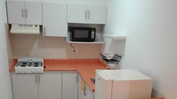 Una cocina funcional con armarios blancos, microondas, cocina a gas y dos taburetes negros.