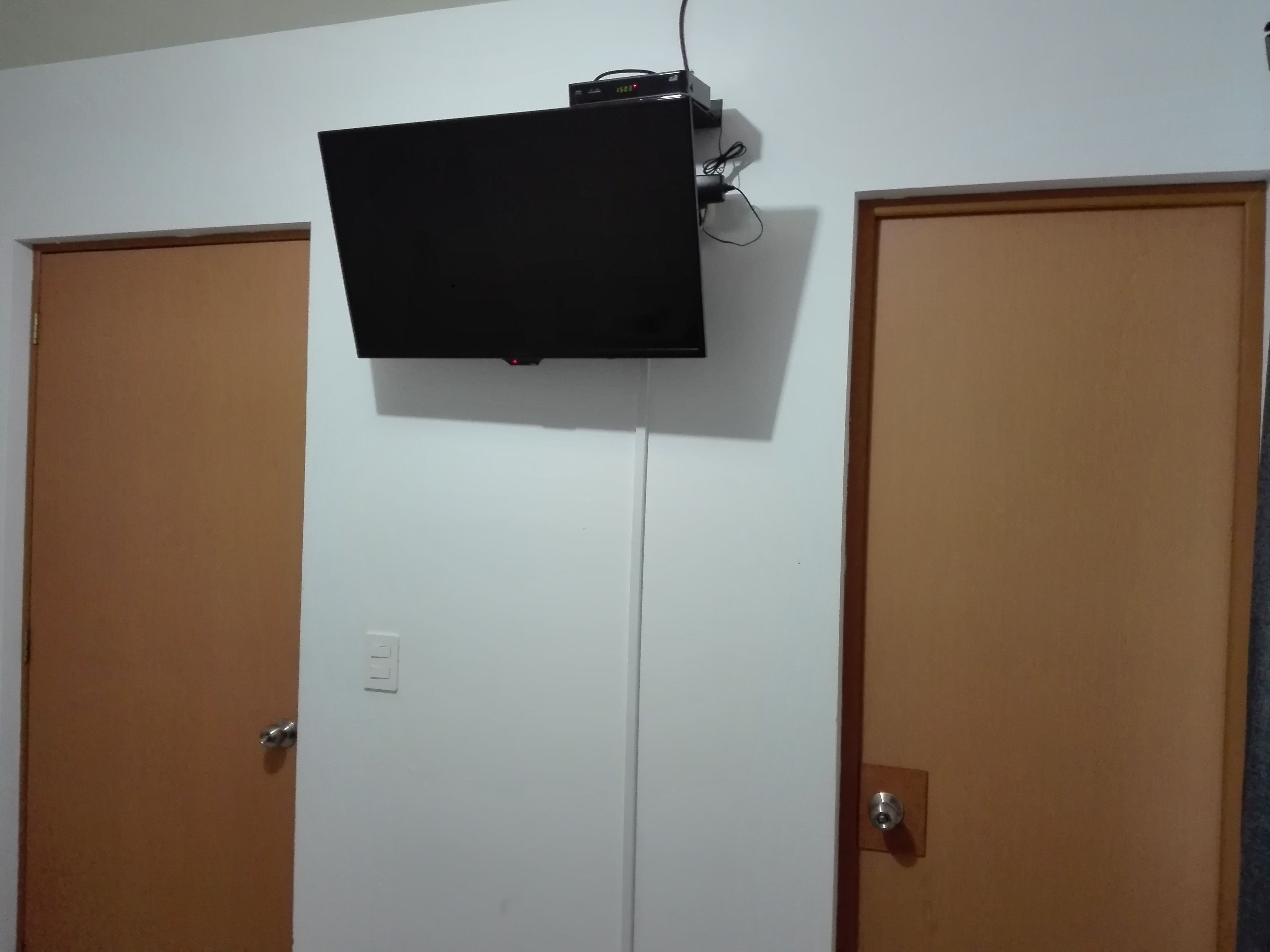 A room with two wooden doors, a mounted television, and a visible electrical outlet.