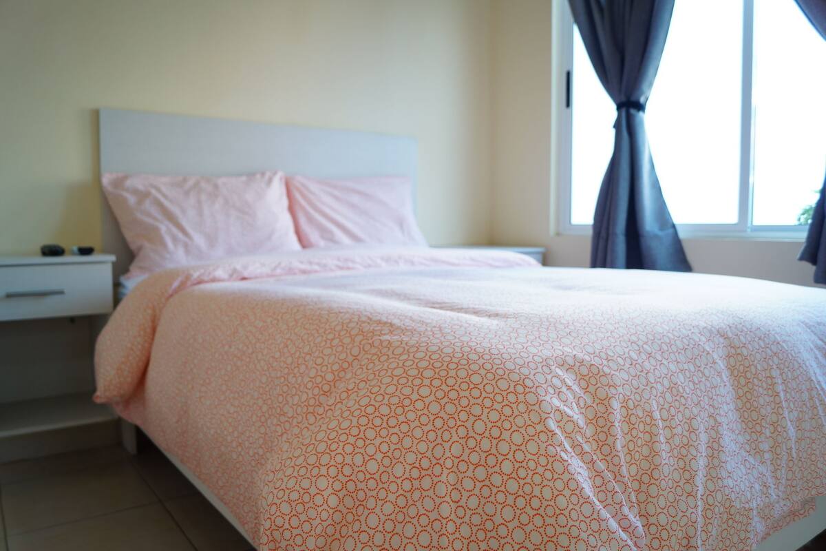 Un dormitorio con cama, mesita de noche y ventana con cortinas.