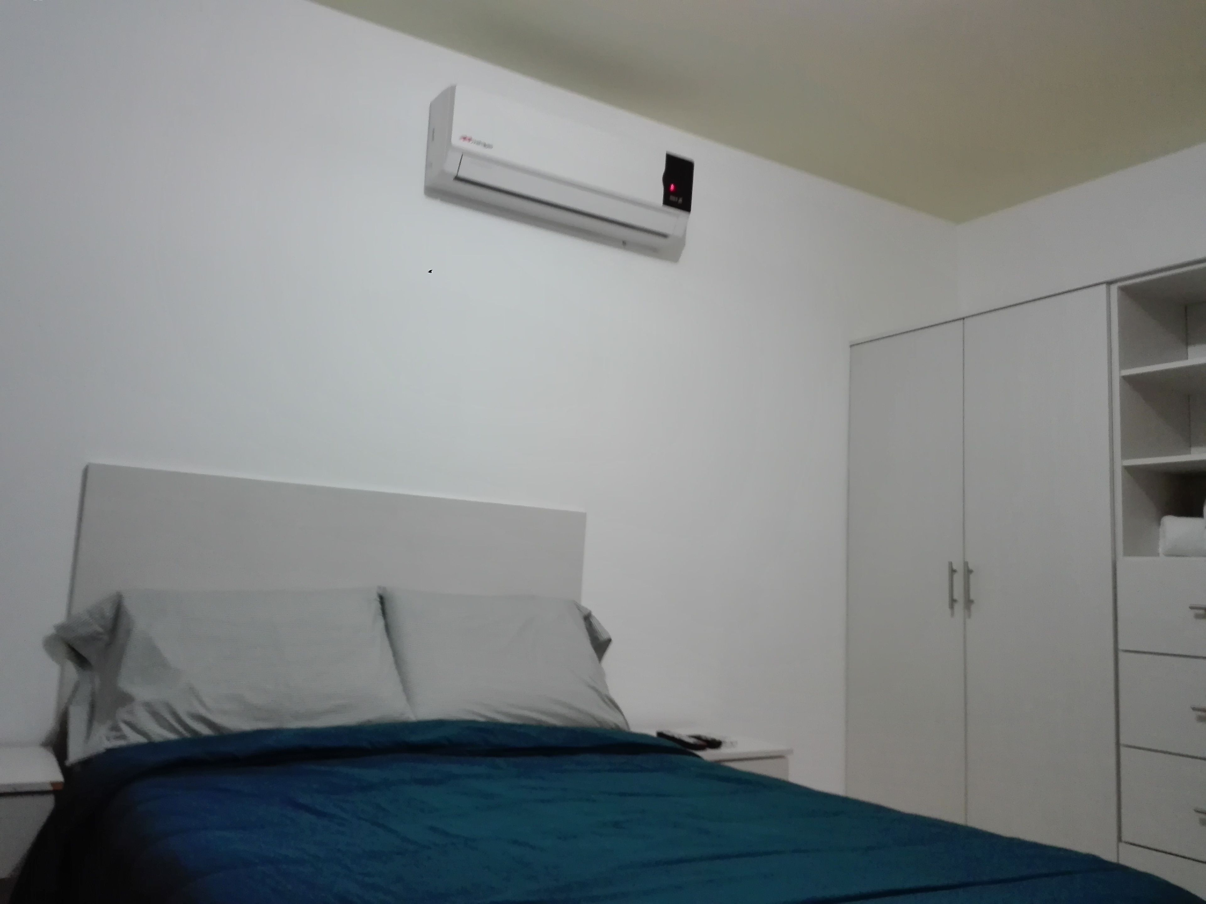 A bedroom with a bed, a white wardrobe, and a wall-mounted air conditioner.