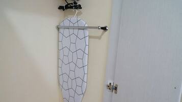 Una habitación con una puerta blanca, un centro de planchado fijado a la pared y una cesta de ropa.