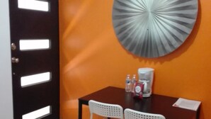 A room with a black door, a round wall decoration, a table with chairs, a coffee maker, and a clock on the wall.